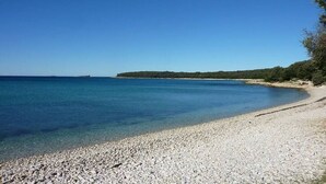 A pebble beach with clear blue water and a distant landmass. - Cottage for 6 persons in Bale near Rovinj (Bale)