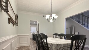 Ein Esszimmer mit einem langen Tisch, Stühlen, einer Chandelier und einer Treppe, die zu einer anderen Ebene führt.