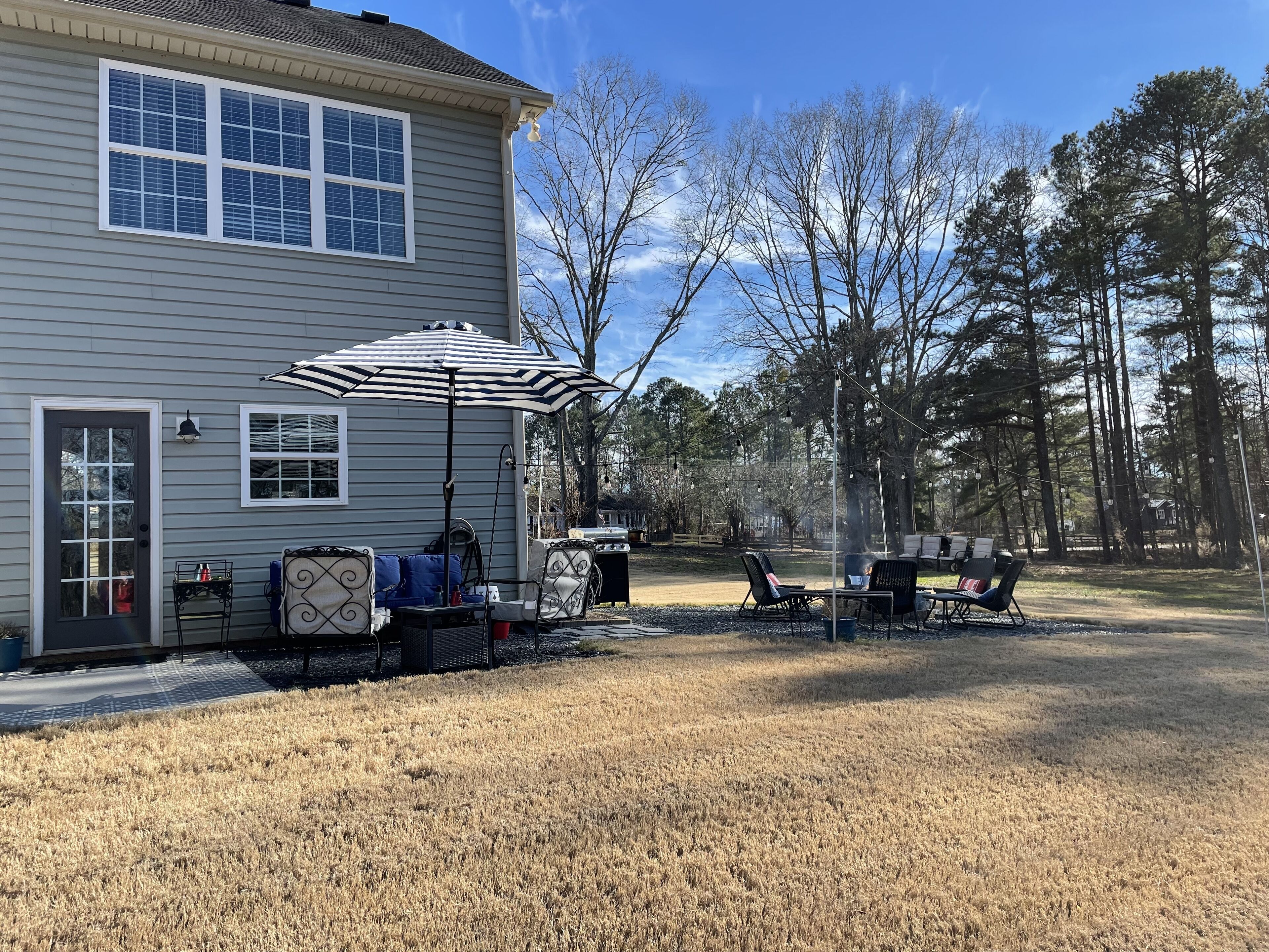 Une maison dotée d’un patio aménagé avec des meubles d’extérieur, un barbecue et un parasol à rayures.
