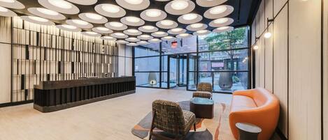 A modern lobby with a reception desk, seating area, and large windows.