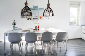A modern dining area with a white table, four grey chairs, and two hanging light fixtures.