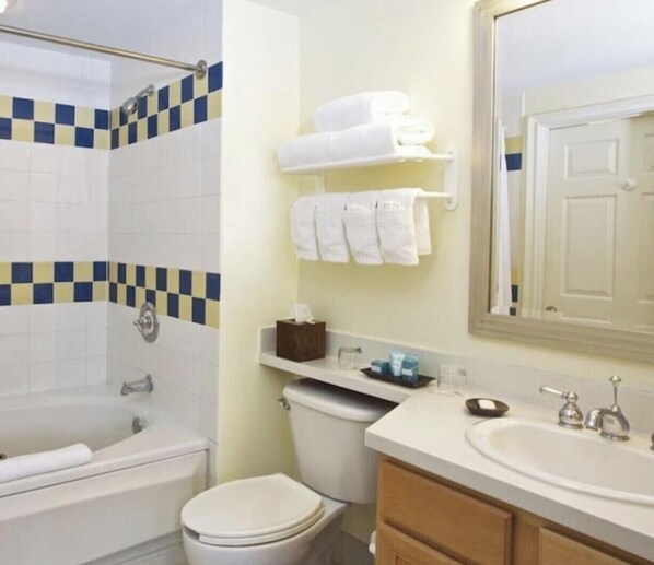 Un bagno con vasca, WC e lavandino. C'è un porta asciugamani con asciugamani e uno specchio sopra il lavandino.