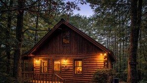 Une cabane en rondins avec un porche, une cheminée et une enseigne sur laquelle on peut lire : « Cree Creek, le lieu hanté ».