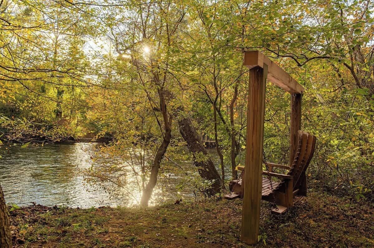 A wooden structure with a bench, surrounded by trees and a body of water.