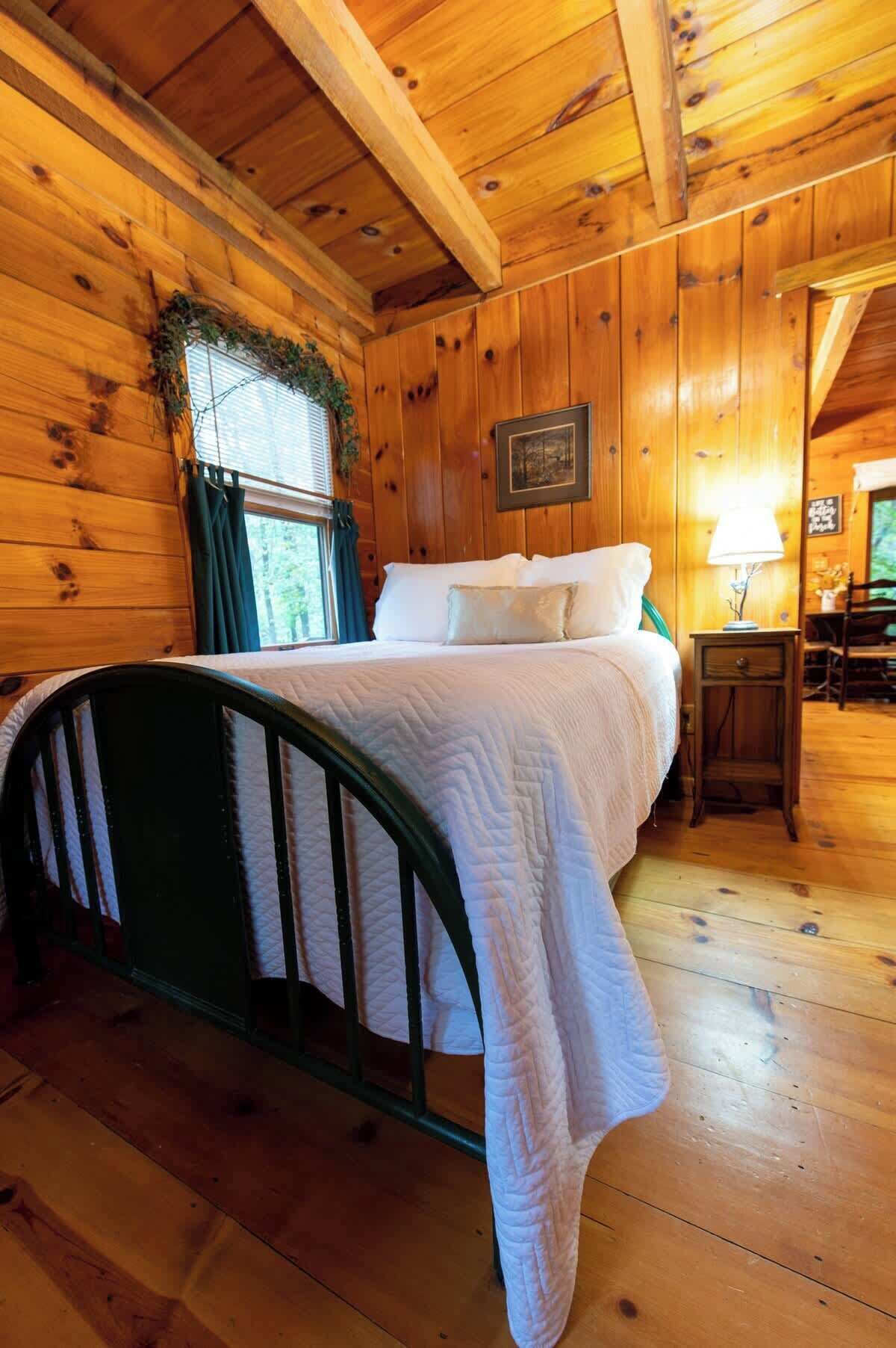 A wooden cabin bedroom with a bed, a nightstand, and a window with curtains.
