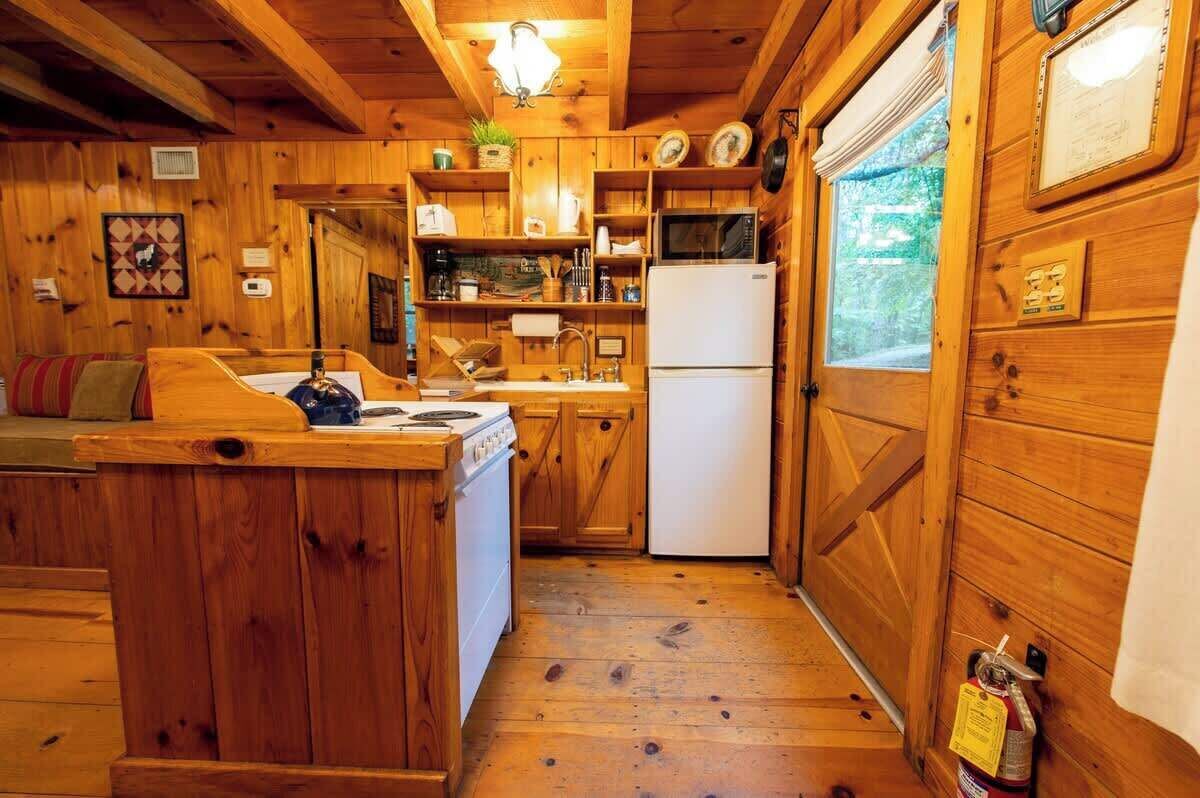 A wooden cabin interior with a kitchen area, including a stove, sink, and refrigerator.