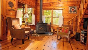 L’intérieur d’une cabane en rondins, avec une cheminée, un plancher en bois, un fauteuil en cuir et un escalier.