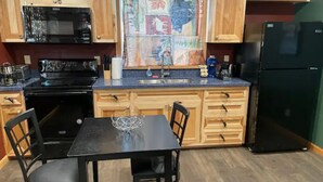 A kitchen with wooden cabinets, a black refrigerator, a microwave, a stove, and a dining table with chairs. - Cedar Mountain - Suite B (Grants Pass)
