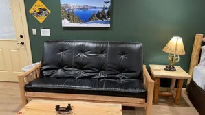A room with a black leather sofa, a wooden coffee table, a lamp, and a framed picture on the wall. - Cedar Mountain - Suite B (Grants Pass)
