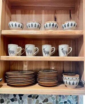 A wooden cabinet with shelves holding ceramic mugs and plates. - Cedar Mountain - Suite B (Grants Pass)