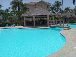 A swimming pool with lounge chairs and a thatched-roof pavilion.