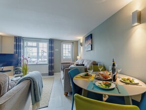 A dining area with a table set for two, a sofa, a TV, and a window with curtains. - 2 bedroom accommodation in Reedham (Reedham)