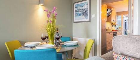 Un comedor con una mesa dispuesta para dos, un florero con flores y un cuadro en la pared.