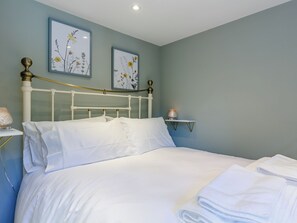 Un lit bien fait, avec du linge de lit blanc, une table de chevet avec une lampe, et deux œuvres d’art florales encadrées accrochées au mur.