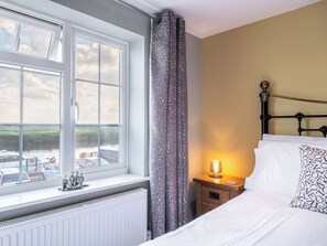 A bedroom with a large window, a bed with white bedding, a bedside table with a lamp, and a radiator. - 2 bedroom accommodation in Reedham (Reedham)
