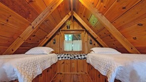 A wooden attic bedroom with two beds, a checkered bench, and a window with curtains. - Ivy quaint tiny cabin creekside - Riverside Resort (Benton)