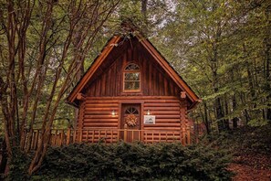 A log cabin with a pitched roof, a central door, and two lit lanterns on either side.