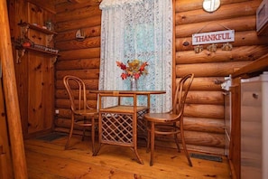 A wooden cabin interior with a table and chairs, a lace curtain, a 'THANKFUL' sign, and a shelf with a 'journey' sign. - Ivy quaint tiny cabin creekside - Riverside Resort (Benton)