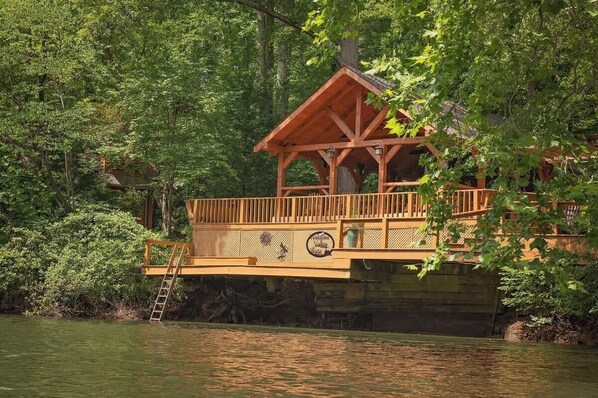 A wooden cabin with a balcony, surrounded by dense forest.