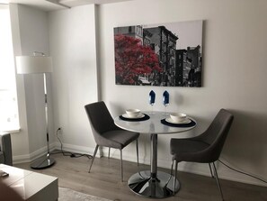 Un comedor moderno con una mesa redonda, dos sillas y una obra de arte con un paisaje urbano en la pared.