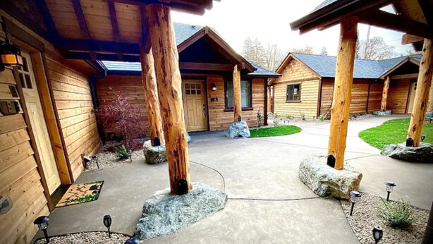 A log cabin-style building with a central courtyard, stone pillars, and a well-maintained lawn. - Cedar Mountain - Suite C (Grants Pass)