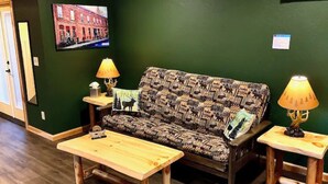 A cozy room with a patterned sofa, two wooden tables, and a television on the wall. - Cedar Mountain - Suite C (Grants Pass)