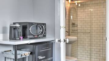 A compact bathroom with a shower, toilet, and a coffee machine on a small shelf.
