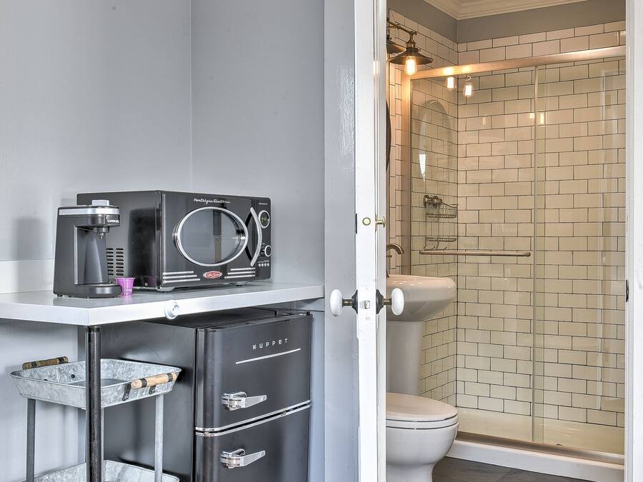 A compact bathroom with a shower, toilet, and a coffee machine on a small shelf.