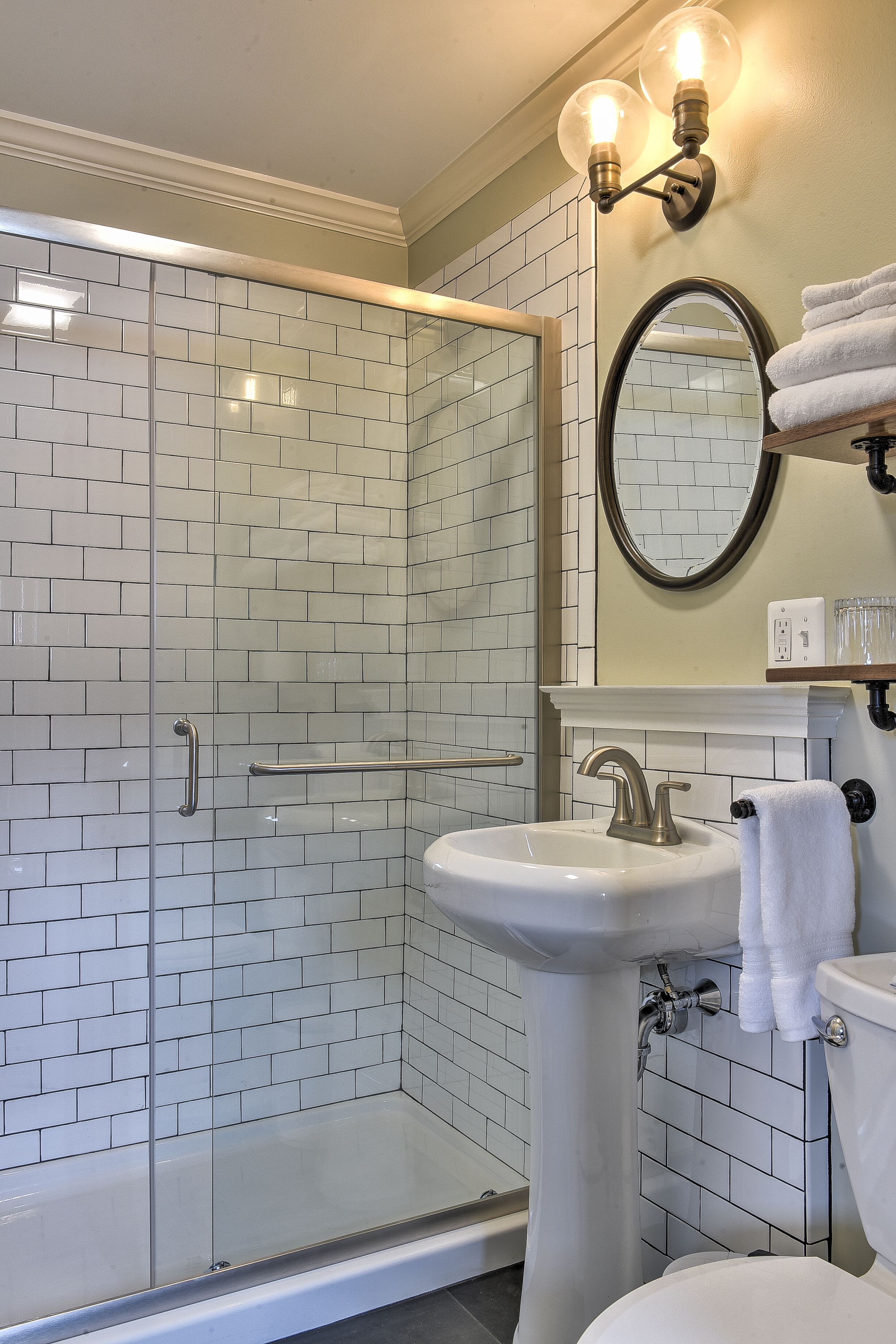 A modern bathroom with a glass-enclosed shower, a pedestal sink, and a toilet.