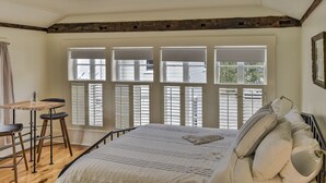 A bedroom with a large bed, a wooden desk, and three chairs. There are three windows with shutters. - The Burrell House (Keene)