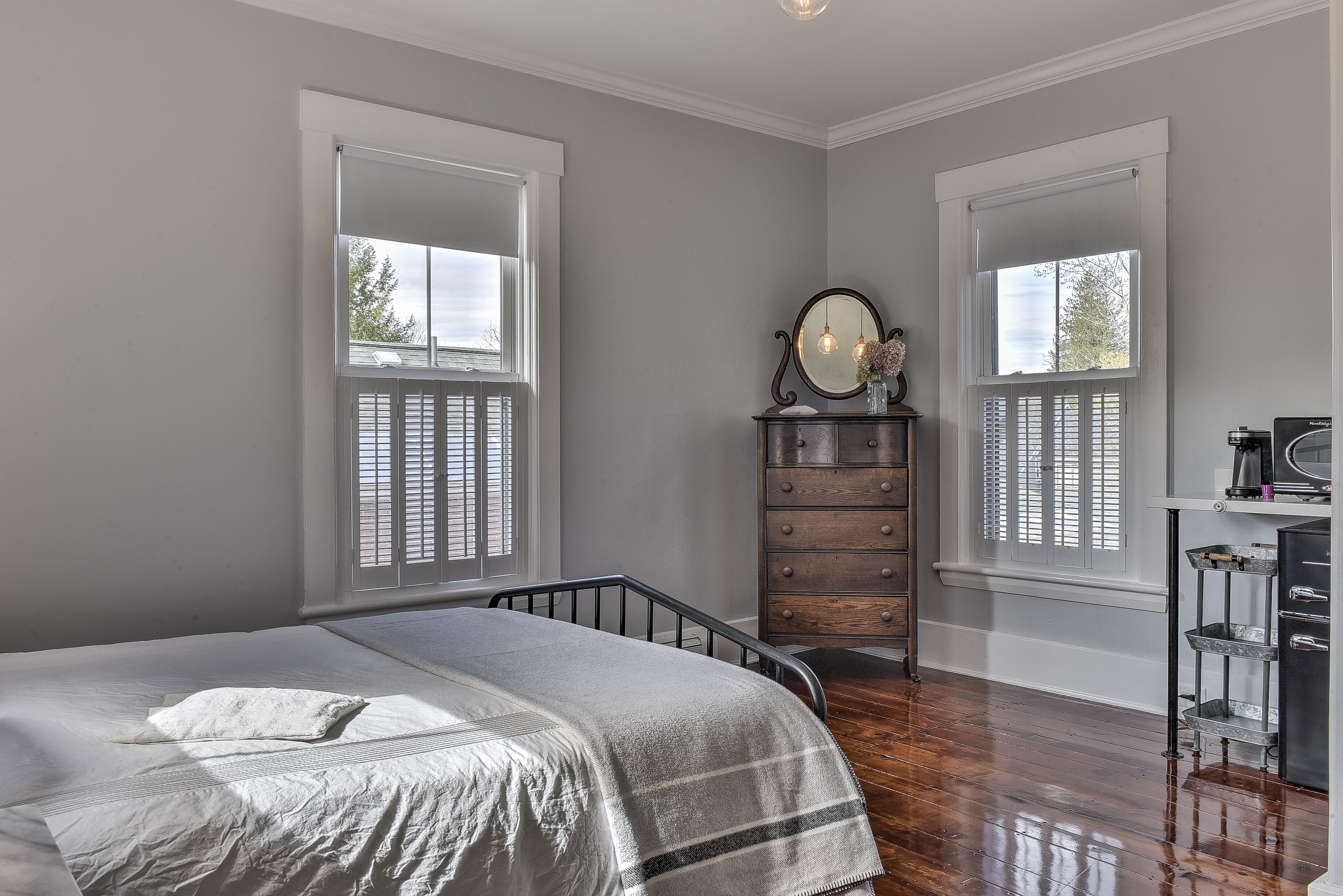 A bedroom with a bed, dresser, and two windows with shutters.