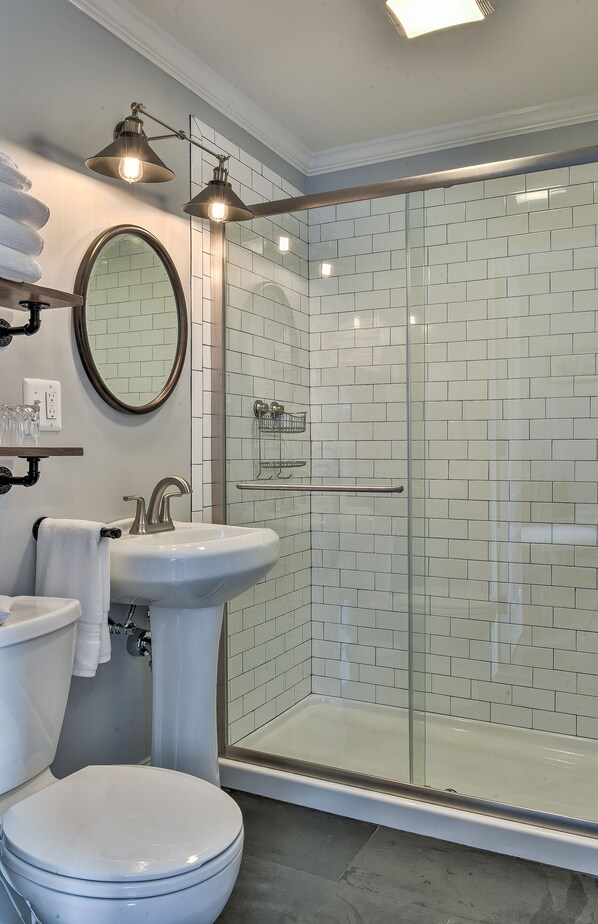 A bathroom with a toilet, sink, and glass-enclosed shower. - The Burrell House (Keene)