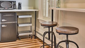A kitchen with a microwave, coffee maker, and a KUPPST refrigerator. There are two stools and a small shelf with a vase. - The Burrell House (Keene)