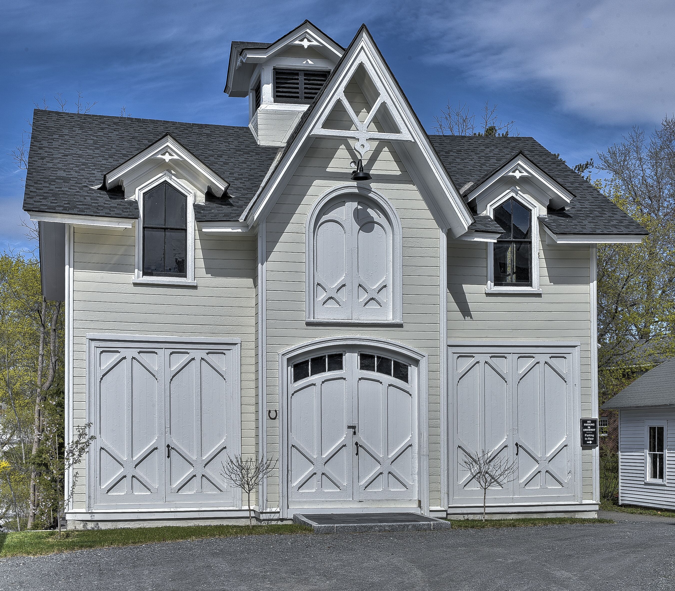 A two-story house with a symmetrical facade, featuring a central entrance with a decorative archway, two garage doors on either side, and a small dormer window on the roof.