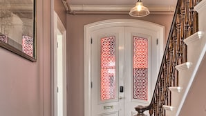 A hallway with a white radiator, a wooden staircase, and a door with decorative glass panels. - The Burrell House (Keene)
