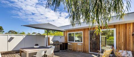 A modern outdoor kitchen area with a wooden deck, a barbecue grill, and a dining table with chairs.
