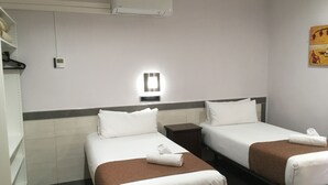 A hotel room with two beds, each with a brown bedspread and white pillows, a small bedside table, a wall-mounted light, and a plain wall with a painting. - Hostal Levante (Barcelona)