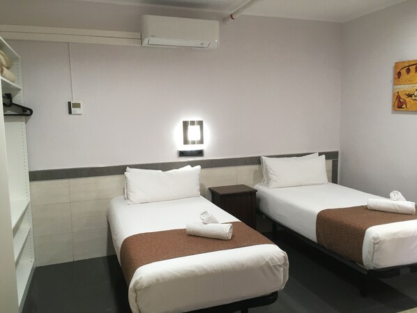 A hotel room with two beds, each with a brown bedspread and white pillows, a small bedside table, a wall-mounted light, and a plain wall with a painting. - Hostal Levante (Barcelona)
