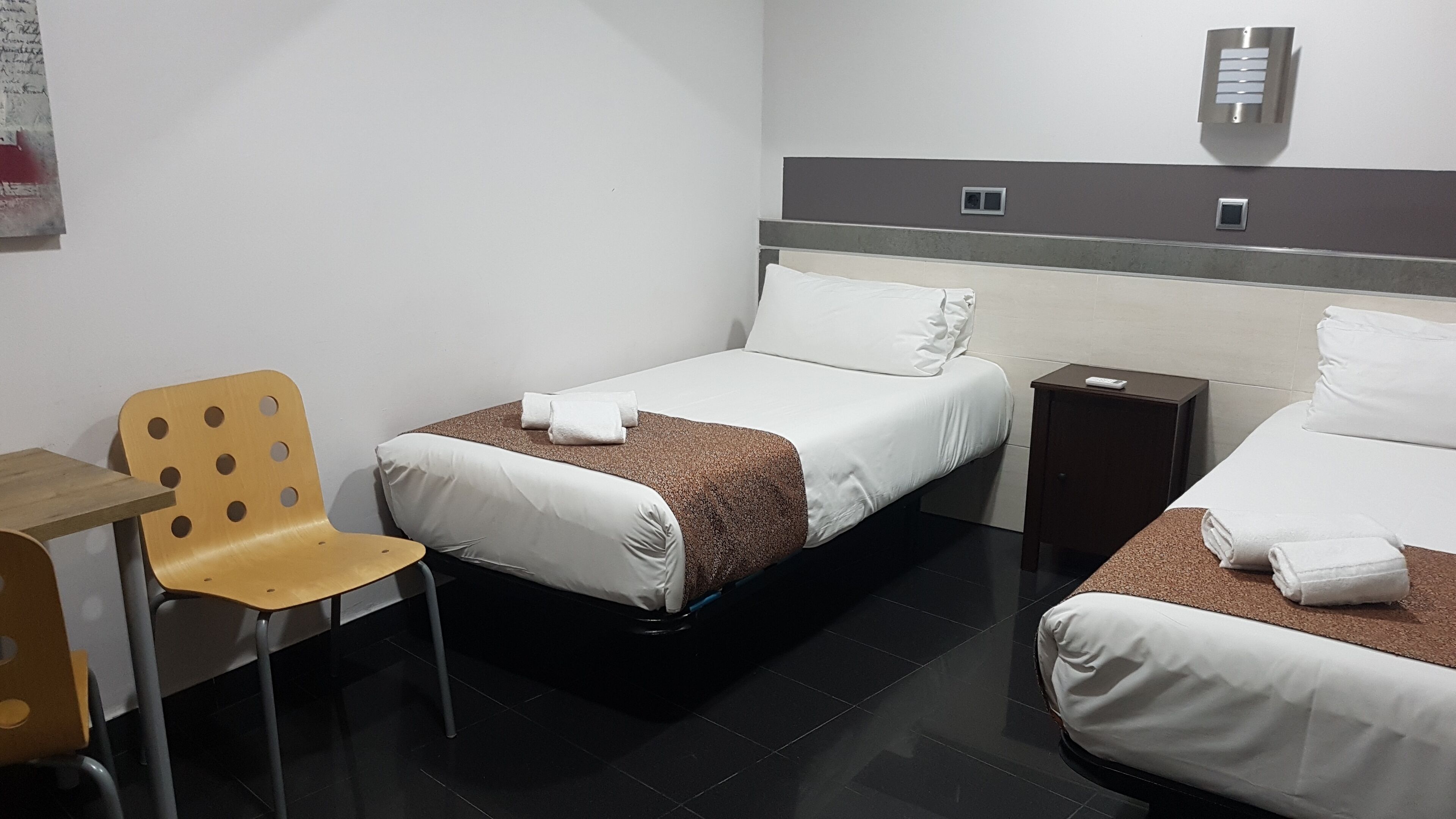 Een hotelkamer met twee bedden, een stoel, een bureau en een klein tafeltje.