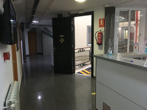 A corridor with a closed door, a fire extinguisher, and a bench. - Hostal Levante (Barcelona)