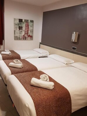 Habitación de hotel con tres camas individuales, cada una con cabecero marrón y ropa de cama blanca. En la pared, hay un cuadro de la Torre Inclinada de Pisa.