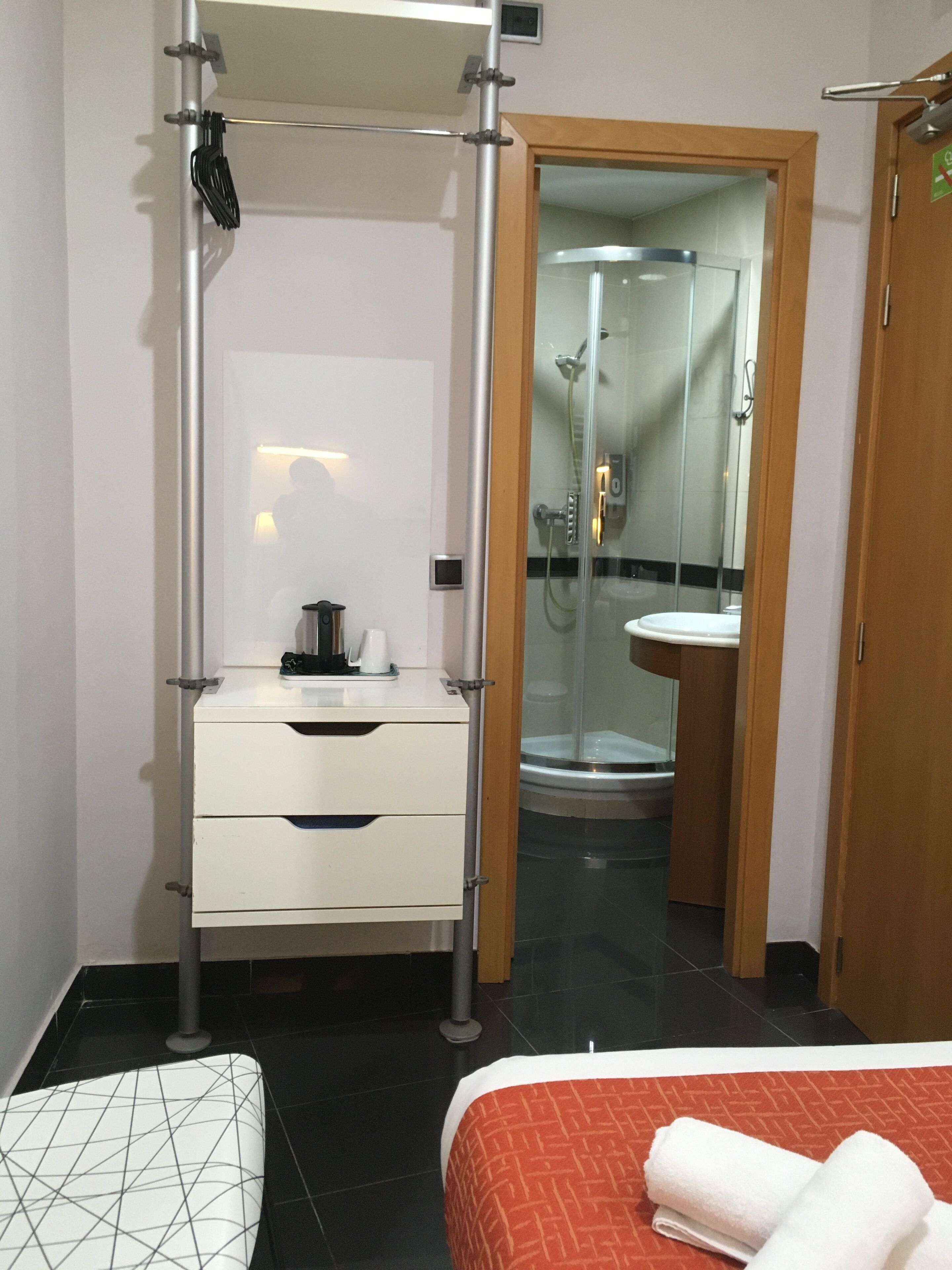 A hotel room with a bed, a bedside table, a mirror, a wardrobe, and a bathroom with a shower and toilet.