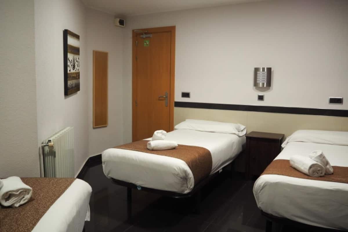 A hotel room with two beds, a wooden door, a radiator, and a towel on the table.