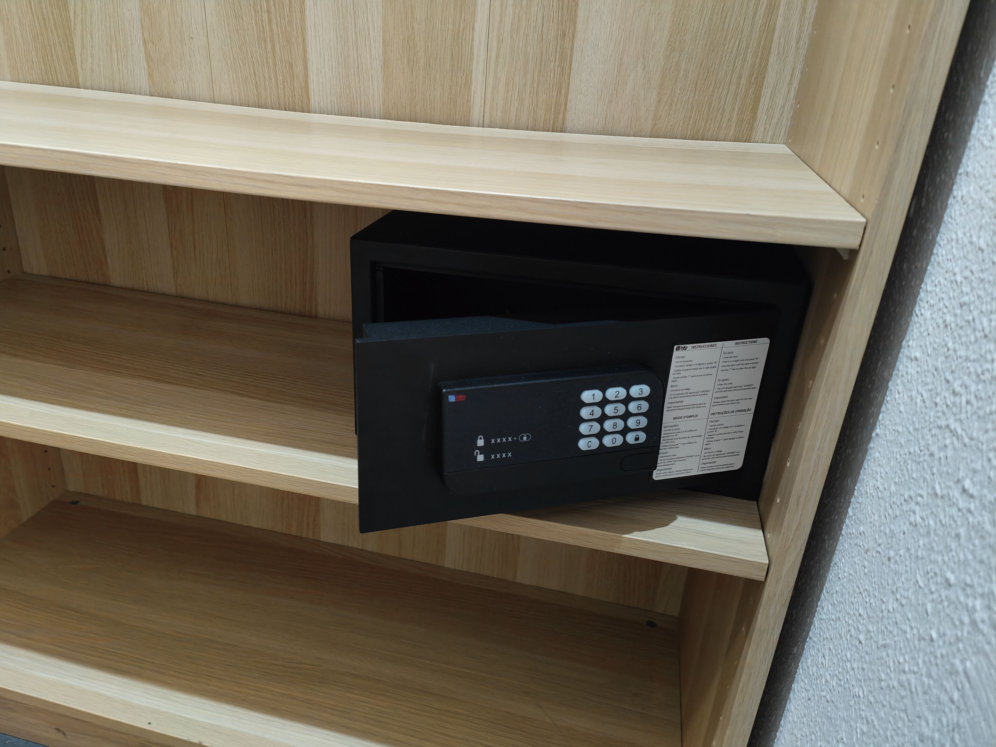 A hotel room with a wooden panel wall and a built-in black safe with a keypad and instructions label.