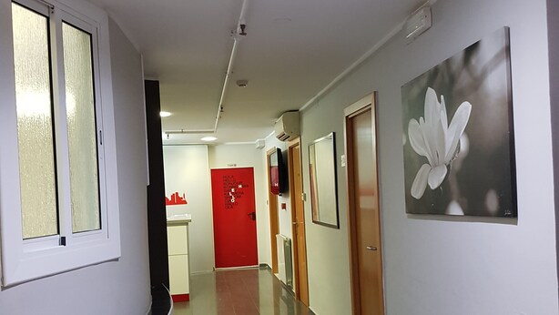 A hallway with a curved wall, a red door, and a framed picture on the wall. - Hostal Levante (Barcelona)