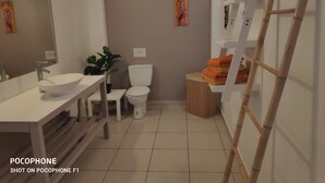 Un baño con lavamanos blanco, inodoro y un pequeño taburete de madera con toallas.