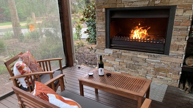 Un espace extérieur accueillant, doté d’une cheminée en pierre, de mobilier en bois et offrant une vue sur un jardin.