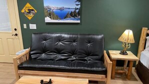 Ein Zimmer mit einer schwarzen Ledersofa, einem Holztisch, einer Lampe und einem gerahmten Bild an der Wand.