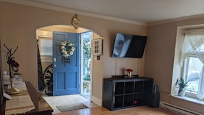 Een woonkamer met een blauwe deur, een flatscreen televisie, een houten vloer en een raam met uitzicht.