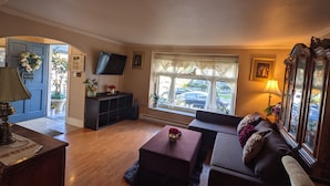 Een woonkamer met een bank, een voetenbankje en een aan de muur bevestigde televisie.